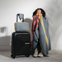 Person wrapped in a chevron design cotton blanket next to a black suitcase with a gray chevron travel pouch on a light background
