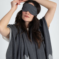 Lady wearing a gray eye mask and gray blanket with heart patterns on a white background