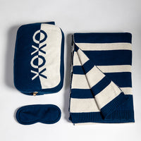 Navy and white striped blanket with XOXO pouch and eye mask on a light gray background