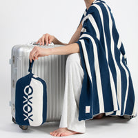 Person holding a silver suitcase with a navy and white bag featuring 'XOXO' design, wearing a blue and white striped blanket.