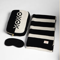 Black and white striped blanket with 'XOXO' pouch and eye mask on a light gray background