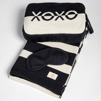 Black and white folded striped blanket with a sleep mask and pouch on a light gray background
