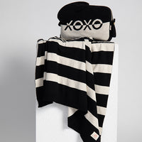 Black and white striped blanket with a eye mask and pouch on a light gray background