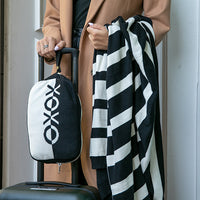 Person holding a black and white striped blanket and a black travel bag with a XOXO logo.