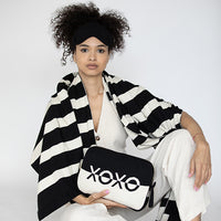 Woman holding a black and white pouch with 'XOXO' text, wearing a black and white striped blanket and black eye mask.