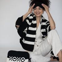 Woman in a white outfit with a black and white striped blanket around her, sitting next to a pouch with 'XOXO' branding.