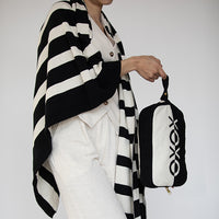 Person holding a black and white bag with 'XOXO' branding and wearing a matching cotton blanket against a plain background