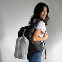 Woman carrying a black and grey backpack with a travel blanket pouch against a plain background.