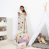 Child holding a colorful heart-patterned blanket in a room with toys and a teepee.