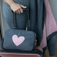 Traveler with carry-on bag and grey and pink reversible travel blanket bag with heart motif.