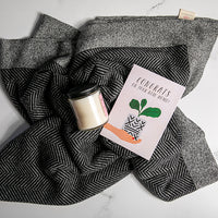Black and white grindle organic cotton blanket with chevron texture knit under a candle and a card on a white surface.