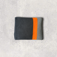 Organic cotton knitted throw blanket in light and dark gray with an orange stripe folded on a textured gray surface.