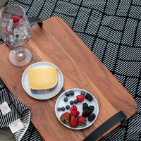 Cotton throw with black and white bricks and dashed designs under a wooden tray with cheese, berries, and a wine glass.