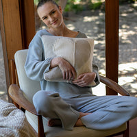 Woman sitting in a chair holding a textured pillow, wearing a light blue outfit.