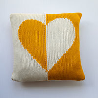 Knitted pillow in tuscansun yellow with a heart design on a white background.