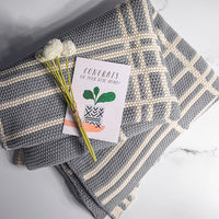 Light gray and white striped and textured cotton blanket with a card and flowers on a light gray background.