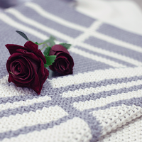 Two red roses placed on a striped double moss knit organic cotton light grey throw blanket.