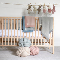 Nursery with wooden crib, colorful blankets, and pastel coloured knot cushions placed on the floor.