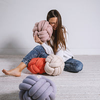 Woman sitting on the floor with knot-shaped cushions in various colors including lavender coral and cream.