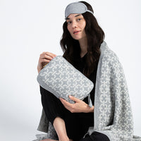 Woman holding a grey chain patterned pouch and wearing a matching eye mask and cotton blanket.