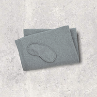 Gray cotton travel blanket with a cotton sleep mask on a textured gray surface.