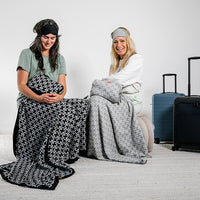 Two cotton travel blanket sets with a link design in black and white being used by two women with suitcases.