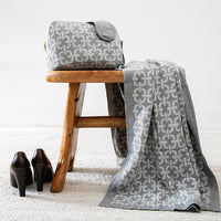 Luxurious zippered compact travel organiser in grey with a chains pattern, holding the matching organic cotton blanket and eye mask set.