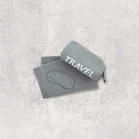 Gray travel set with words 'Travel' in mint green pouch and eye mask on a textured gray surface
