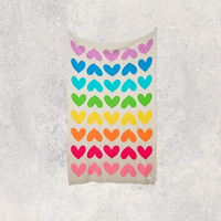 Luxurious cotton blanket with rainbow coloured hearts on a textured white background.