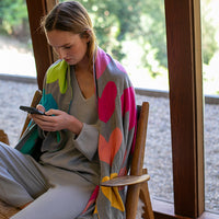 Woman sitting on a chair with a colorful blanket, using a phone.