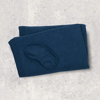 Folded navy blue organic cotton blanket with navy blue eye mask on a light gray textured surface.