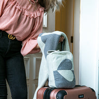 Person with a pink blouse and Gucci belt standing next to a suitcase with a patterned bag and cotton blanket on top.