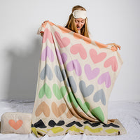 Woman holding a colorful heart-patterned blanket on a bed.