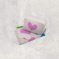 Gray pouch with pink heart and matching pouch and eye mask on a textured gray surface.