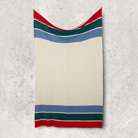 Beige cotton blanket with red, green, and blue stripes stretched on a textured gray background.