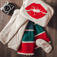 Folded blanket pouch with red lip print, striped blanket, and camera on a wooden surface.