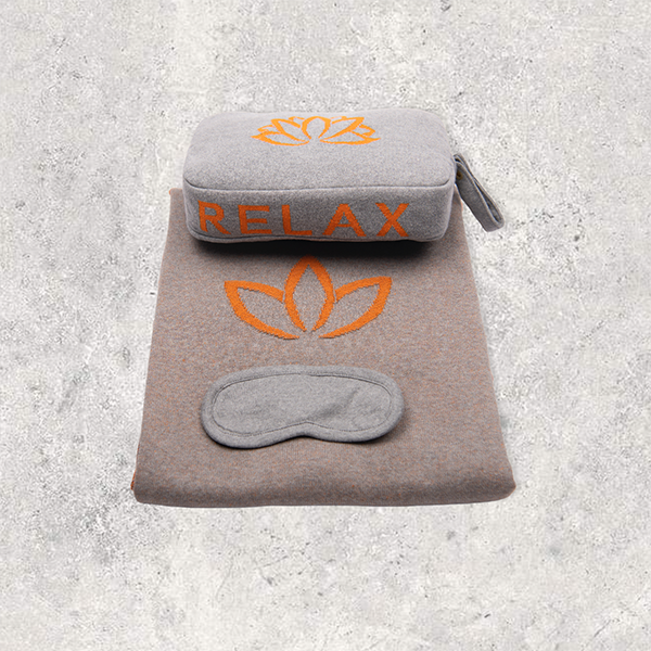 Travel blanket with a lotus and a pouch with 'RELAX' logo and eye mask on a textured surface.