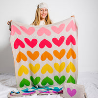Person wearing an eye mask and holding a colorful heart-patterned cotton blanket with a plain background.
