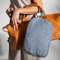 Person holding a brown leather bag with a blue and grey shaded cotton pouch on a plain background