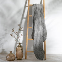 Ash colour textured throw blanket draped over a wooden ladder with decorative vases on a light background.