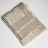 A linen sand beige and white textured cotton throw with a thick beige border folded on a plain white background.