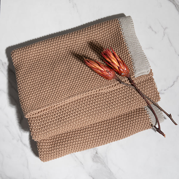 Knitted linen brown cotton blanket with a branch and flowers on a light background.