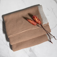Knitted linen brown cotton blanket with a branch and flowers on a light background.