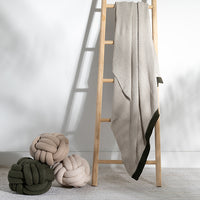 Decorative knit throw blanket in sand colour draped on a ladder next to three knot pillows.