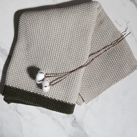 Folded cotton knit throw blanket with a dark border with a decorative plant on a marble surface.