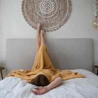 Person lying on a bed with a yellow blanket, feet raised, against a decorative wall mandala.