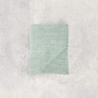 Moss knitted throw blanket on a textured gray background.