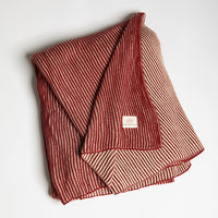 Folded red and white striped textured blanket photographed on a light gray background.