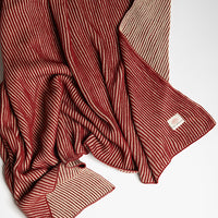 Red and beige striped marsala cotton throw with a Pink Lemonade brand label stitched in the corner laid on a white background.