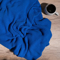 Marine blue knitted cotton blanket on a wooden surface next to a cup of coffee.